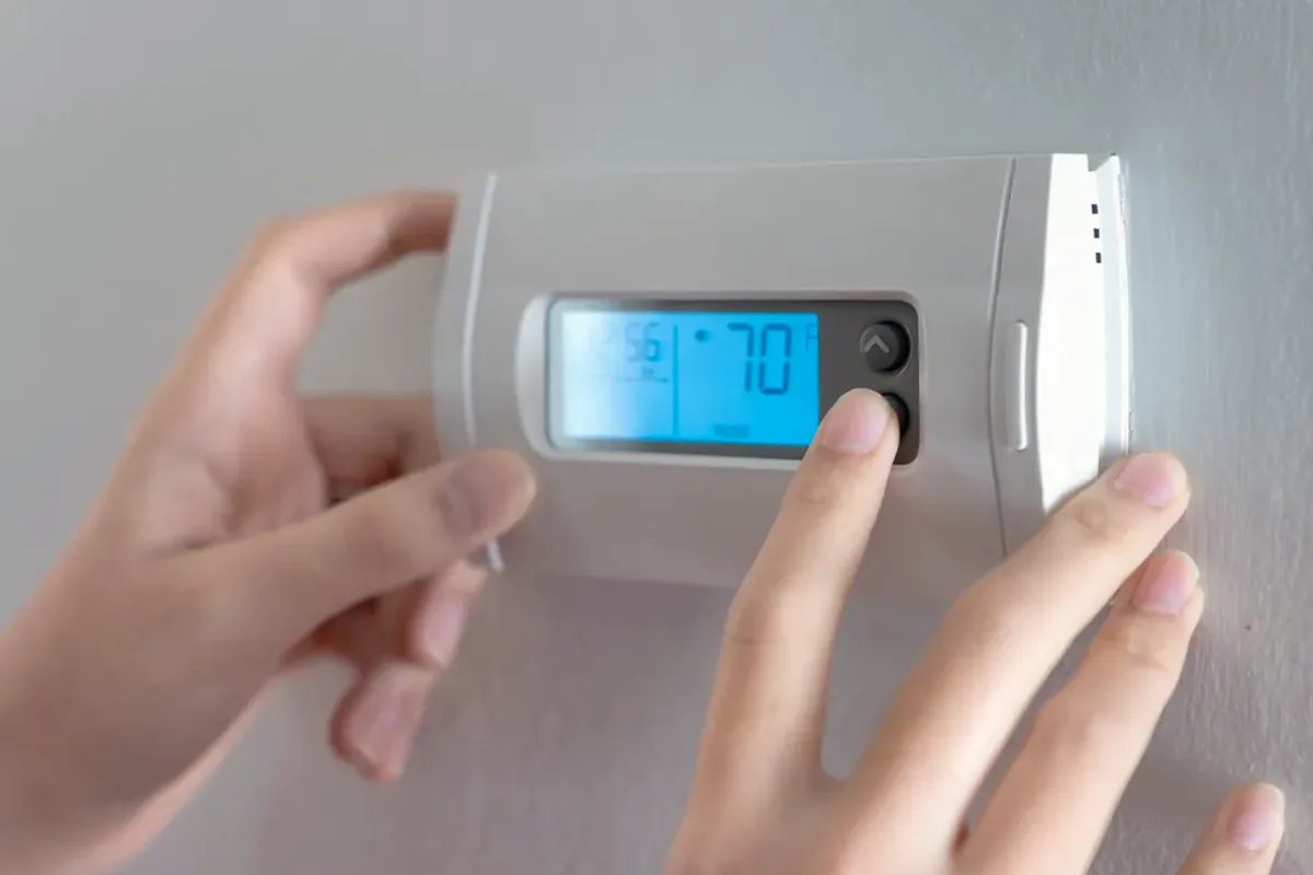 Hands adjusting a digital wall thermostat