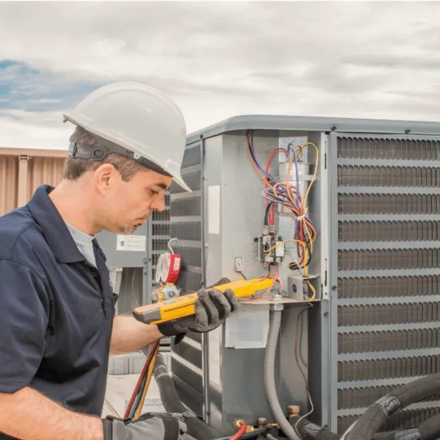 HVAC technician in a hard hat testing an outdoor air conditioner with a multimeter